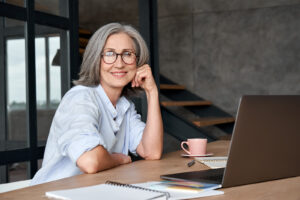 A smiling, attractive mature woman sitting at her computer