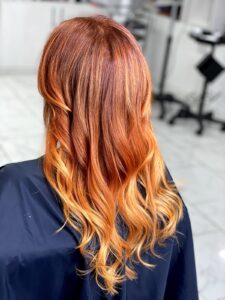 Woman sitting in a beauty salon with beautiful long red dyed hair with subtle blonde highlights at the ends